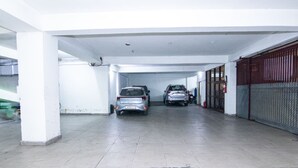 A covered parking area with two cars parked, white pillars, and a red gate on the right. - Hotel Vinayak (Haridwar)