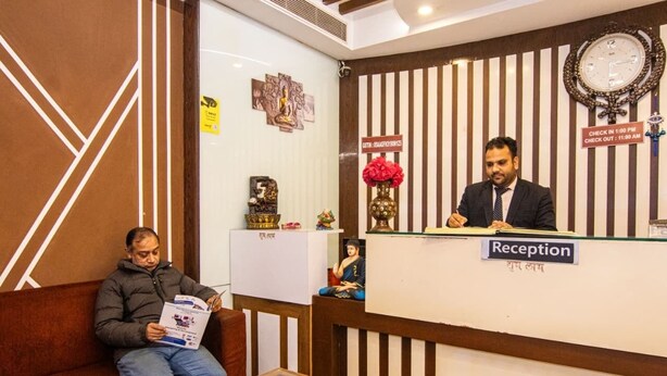 A reception area with a reception desk, a clock, and a sign indicating check-in and check-out times. - Hotel Vinayak (Haridwar)