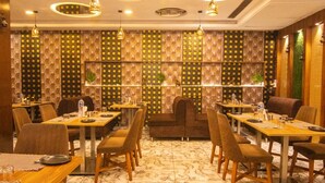 A restaurant with a patterned wall, round ceiling lights, and a marble floor. - Hotel Vinayak (Haridwar)