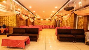 A banquet hall with a central seating arrangement, tables, and draped curtains. - Hotel Vinayak (Haridwar)