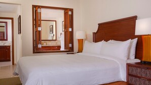 Habitación de hotel con una cama grande, cabecera de madera, mesita de noche con lámpara y un espejo que refleja la habitación.