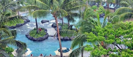 A tropical resort with a central pool surrounded by palm trees and rock formations.