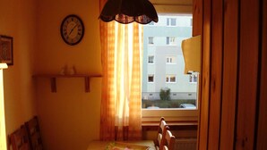 A small dining area with a table, chairs, a clock, and a window with curtains. - Apartment Bulang (Karlshagen)