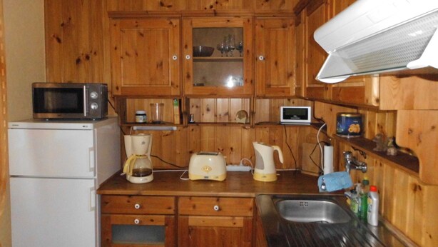 A compact kitchen with wooden cabinets, a microwave, a coffee maker, a toaster, and a sink. - Apartment Bulang (Karlshagen)