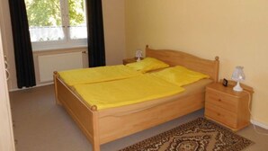 A bedroom with a wooden bed, a nightstand, a lamp, and a window with curtains. - Apartment Bulang (Karlshagen)