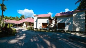 A row of white buildings with red roofs, likely part of a resort or hotel, surrounded by palm trees and a clear sky. - Bowfin Resort (Port Blair)