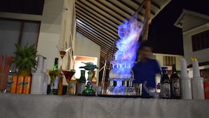 A bar area with a variety of bottles and glasses, including a flaming glass. - Bowfin Resort (Port Blair)