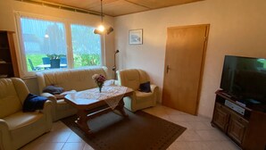 A living room with a sofa set, a coffee table, a TV, and a sliding glass door to the outside. - Holiday house No. 5 - Rügen-Fewo 102 (Sagard)