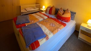 A bedroom with a bed, a crib, a nightstand, and a wall-mounted picture. - Holiday house No. 5 - Rügen-Fewo 102 (Sagard)