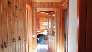 Un couloir en bois avec une porte donnant sur une pièce dotée d’une fenêtre et d’une chaise.