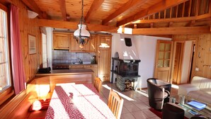 Un vaste espace de vie doté d’un plafond en bois, d’une table à manger recouverte d’une nappe rouge et blanche, et d’une cheminée.