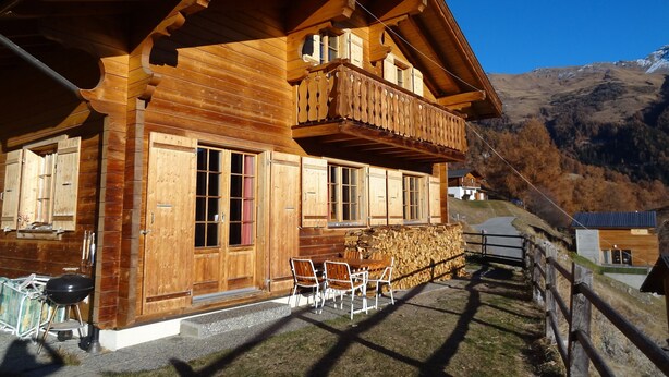 Un chalet en bois doté d’un balcon, d’un coin repas avec des chaises et d’une pile de bois de chauffage.