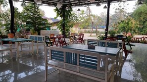 An outdoor seating area with tables and chairs, surrounded by greenery and trees. - Baan Suan San Rak (Buriram)