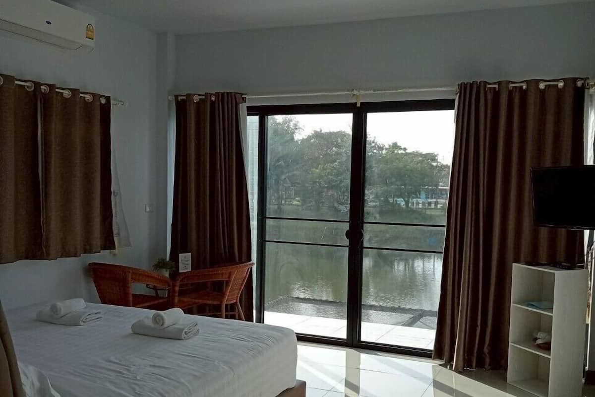 A hotel room with a large bed, a desk, a chair, a TV, and a view of a body of water through a glass door.
