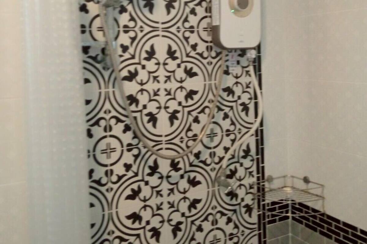 A bathroom with a patterned tile wall, a shower with a hose, and a soap dispenser.