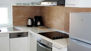 A modern kitchen with white cabinets, a stainless steel refrigerator, a built-in oven, and a coffee maker. - House Ercegovic A2 + 2 (Primošten)