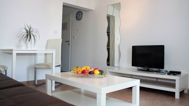 A modern living room with a white sofa, a dining table with chairs, a fruit bowl, a TV on a white stand, and a large mirror. - House Ercegovic A2 + 2 (Primošten)