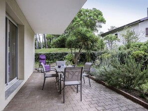 A patio with a table and chairs, surrounded by greenery and a building. - Tassigny by Interhome (Capbreton)