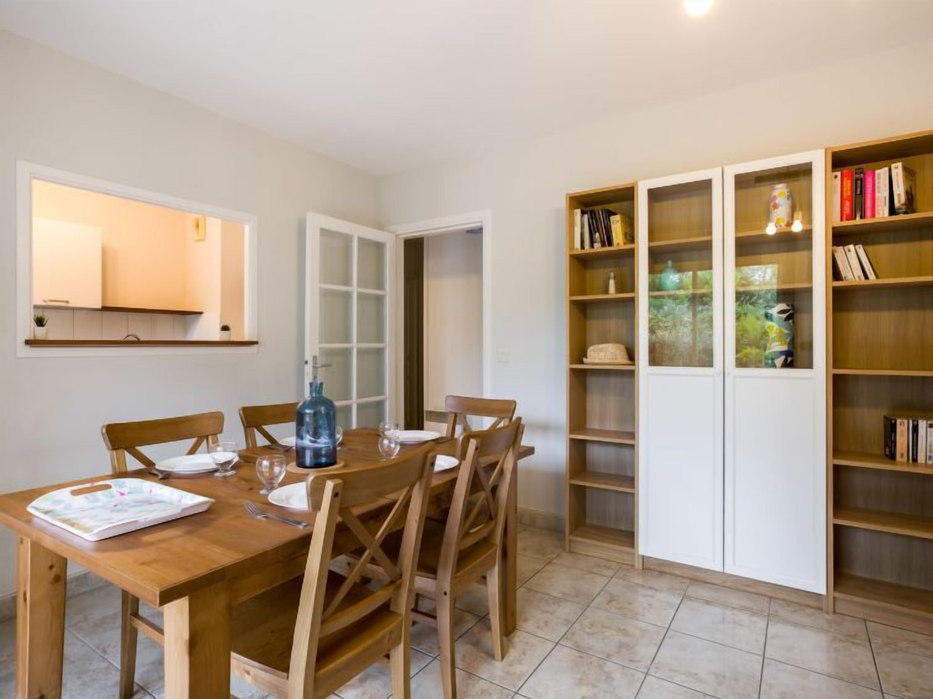 Un coin repas avec une table et des chaises en bois, une bibliothèque remplie de livres et d’objets décoratifs, et une porte donnant sur une autre pièce.