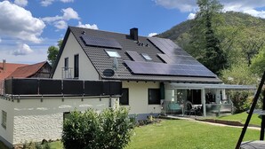 A modern house with solar panels, a covered patio, and a view of a mountain.