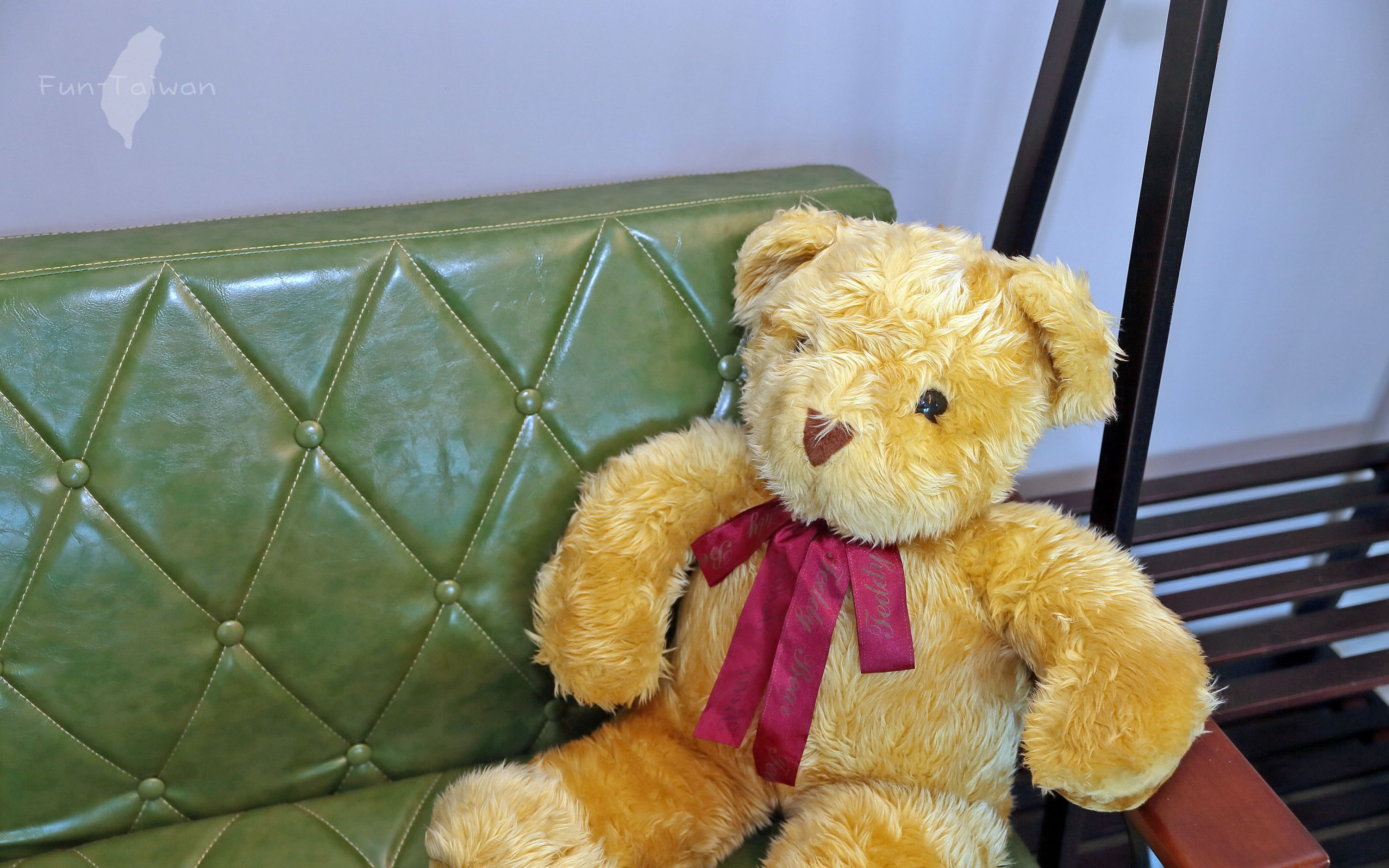 A teddy bear sitting on a green upholstered bench.