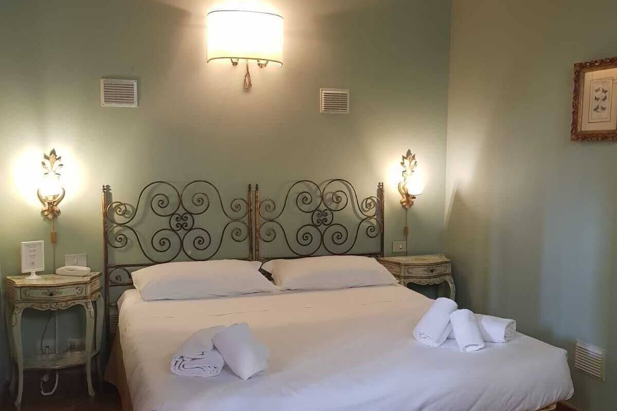 A neatly made bed with white linens, two bedside tables with lamps, and a wall-mounted light fixture.
