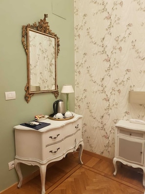 A room with a white vanity, a mirror with an ornate frame, a small table with a lamp, and floral wallpaper. - Hotel Il Granduca (Florence)