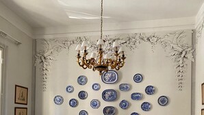 Un comedor con sillas y mesas blancas, una araña y platos decorativos azules y blancos en la pared.
