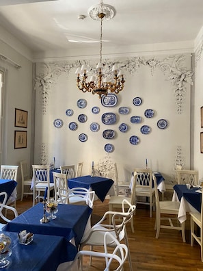 A dining area with white chairs and tables, a chandelier, and blue and white decorative plates on the wall. - Hotel Il Granduca (Florence)