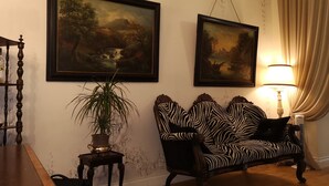 Una habitación con dos cuadros enmarcados, un sofá estampado con diseño de cebra, una mesita con una planta y una lámpara.