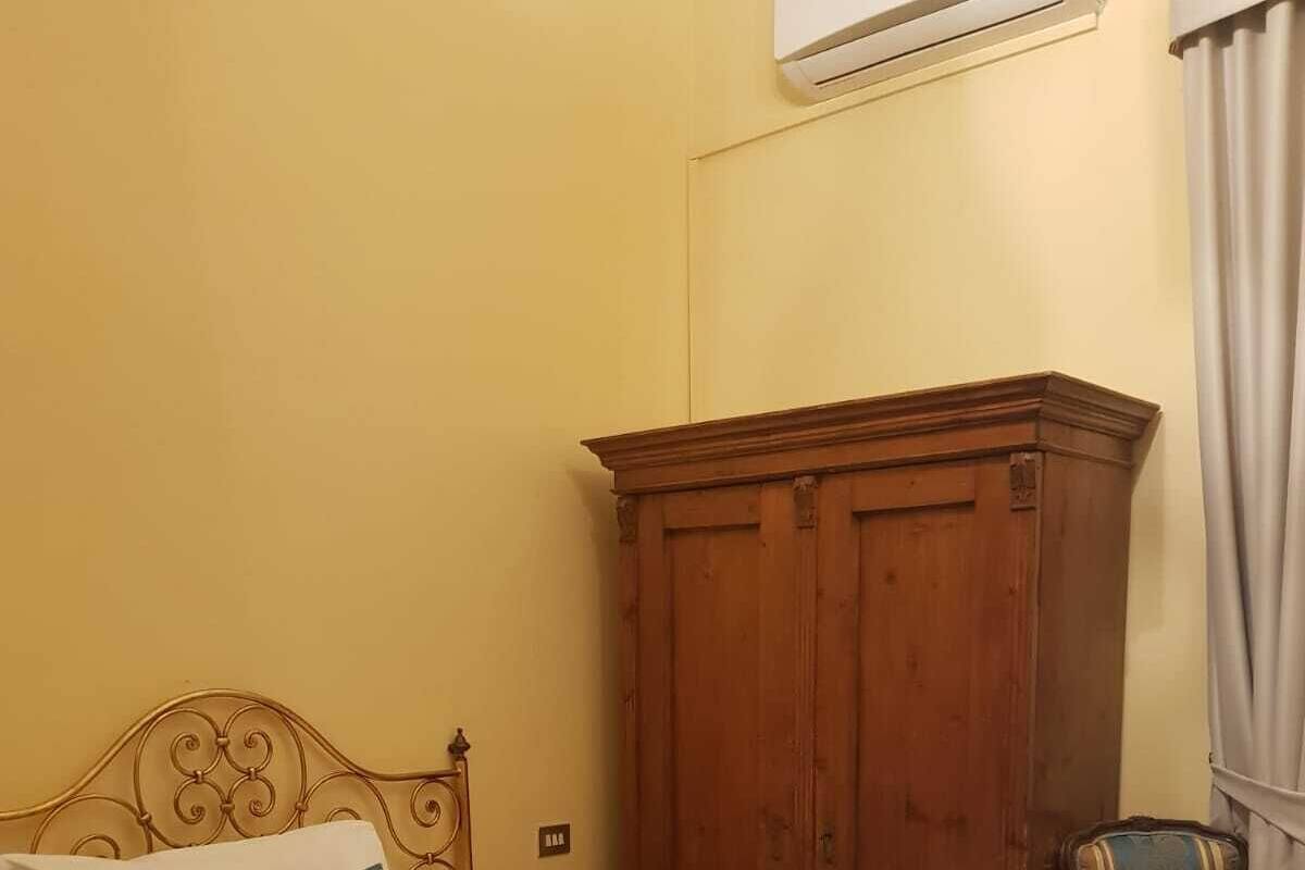 A neatly made bed with a blue and white bedspread, a wooden wardrobe, and a chair with a floral pattern.