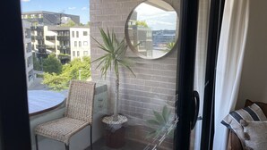 A balcony with a wicker chair, a potted plant, and a round mirror on the wall. - Self-contained one bedroom apartment - Kingston Foreshore on your doorstep (Kingston)