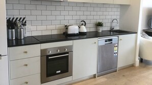 A modern kitchen with white cabinets, a black countertop, a stainless steel oven, a dishwasher, and a kettle. - Self-contained one bedroom apartment - Kingston Foreshore on your doorstep (Kingston)