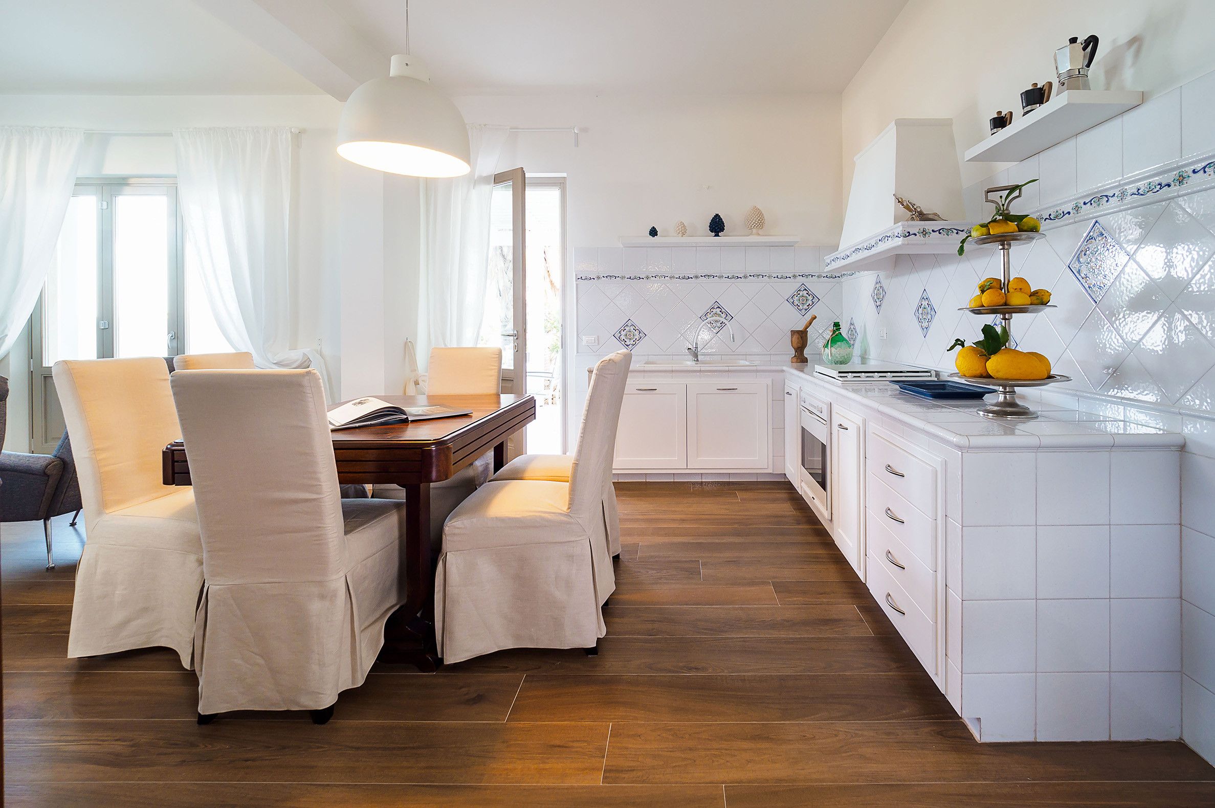 A modern kitchen with white cabinetry, a dining area with two chairs, and a wooden floor.