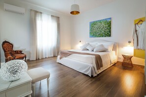 A bedroom with a bed, bedside lamps, a chair, a round table, and a painting on the wall.