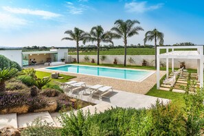 A modern outdoor pool area with a clear view of the landscape, a seating area, and a pergola structure.