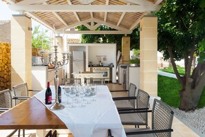 An outdoor dining area with a covered patio, a stone wall, and a grill station.