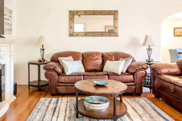 A living room with a brown leather sofa, a round wooden coffee table, and two small side tables with lamps. - Downtown Santa Fe, Walk to Plaza, 2B / 2B + Full Kitchen, AIr Conditioned (Santa Fe)