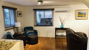 Un salon avec un parquet en bois, un fauteuil bleu, un canapé foncé et une petite table sur laquelle se trouve un vase.