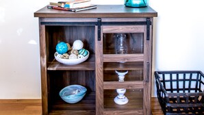 Un meuble en bois avec des portes en verre, un vase turquoise orné de branches et un tableau encadré accroché au mur.