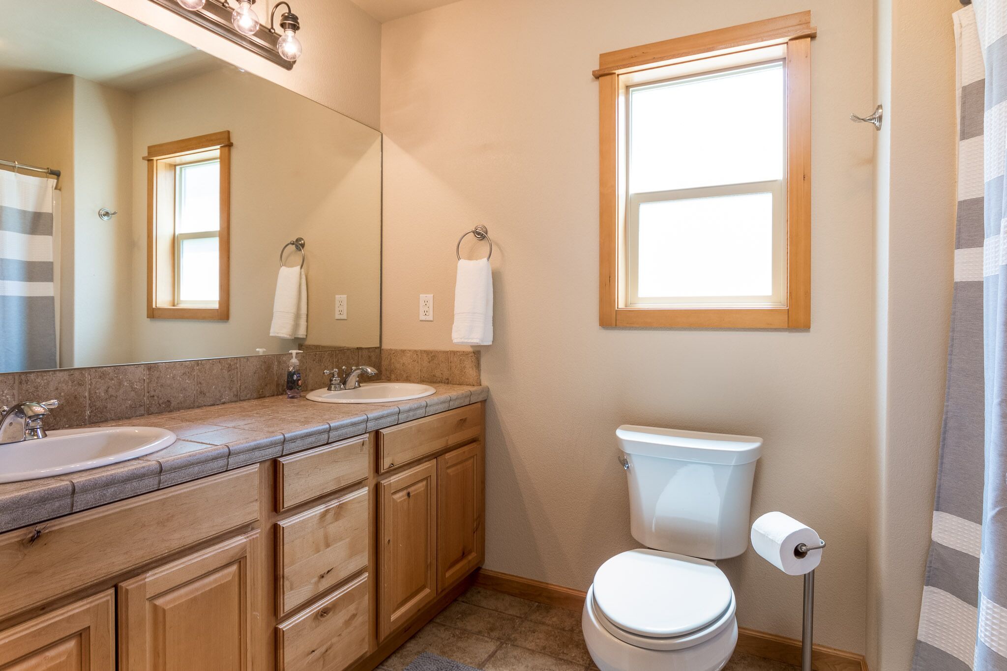 A bathroom with a wooden vanity, two sinks, a toilet, and a window.