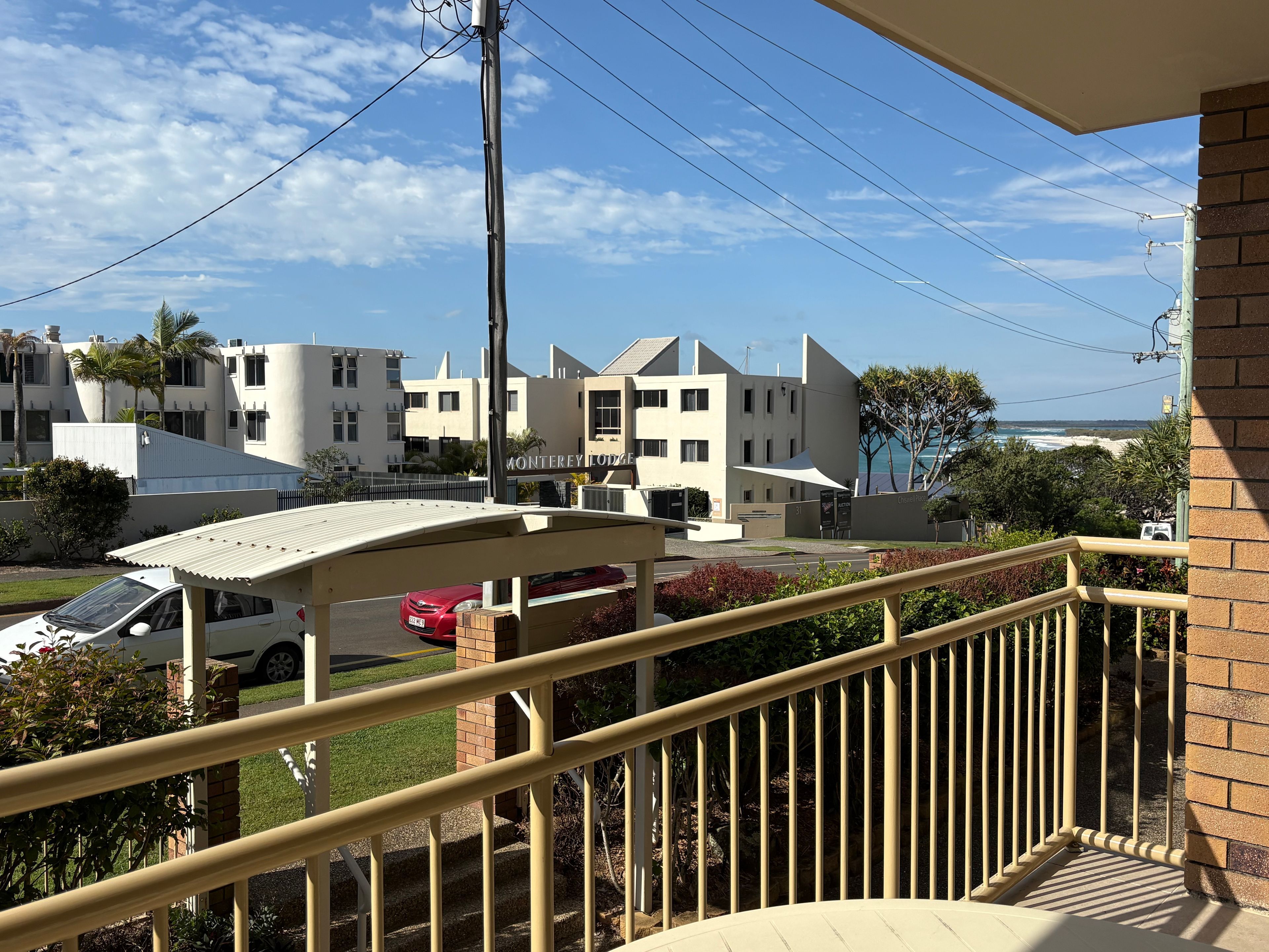 A hotel with a covered parking area, a balcony with a railing, and a view of the ocean.
