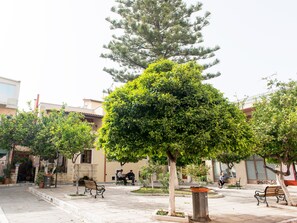 A courtyard with benches, trees, and a building with a tiled roof. - Mat Old Town Apartments (Rethymno)