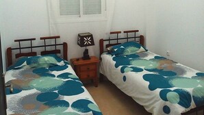 A small, clean room with two single beds, a nightstand with a lamp, a window with curtains, and a chandelier. - Chic appartment with swimming pool (Tanger)