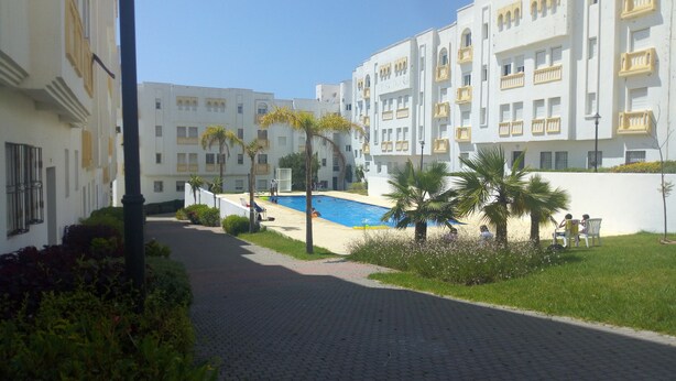 A courtyard with a swimming pool, palm trees, and a paved walkway. - Chic appartment with swimming pool (Tanger)