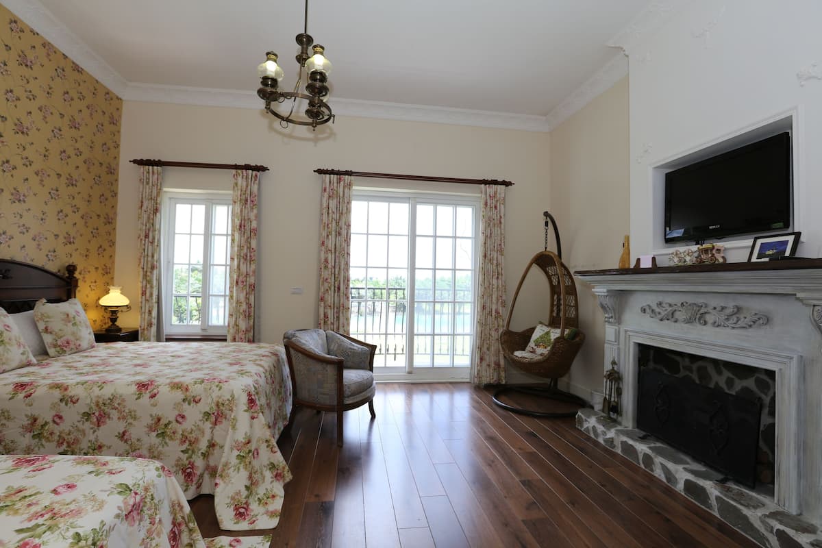 Un dormitorio con dos camas, chimenea, televisor y una ventana grande con cortinas.