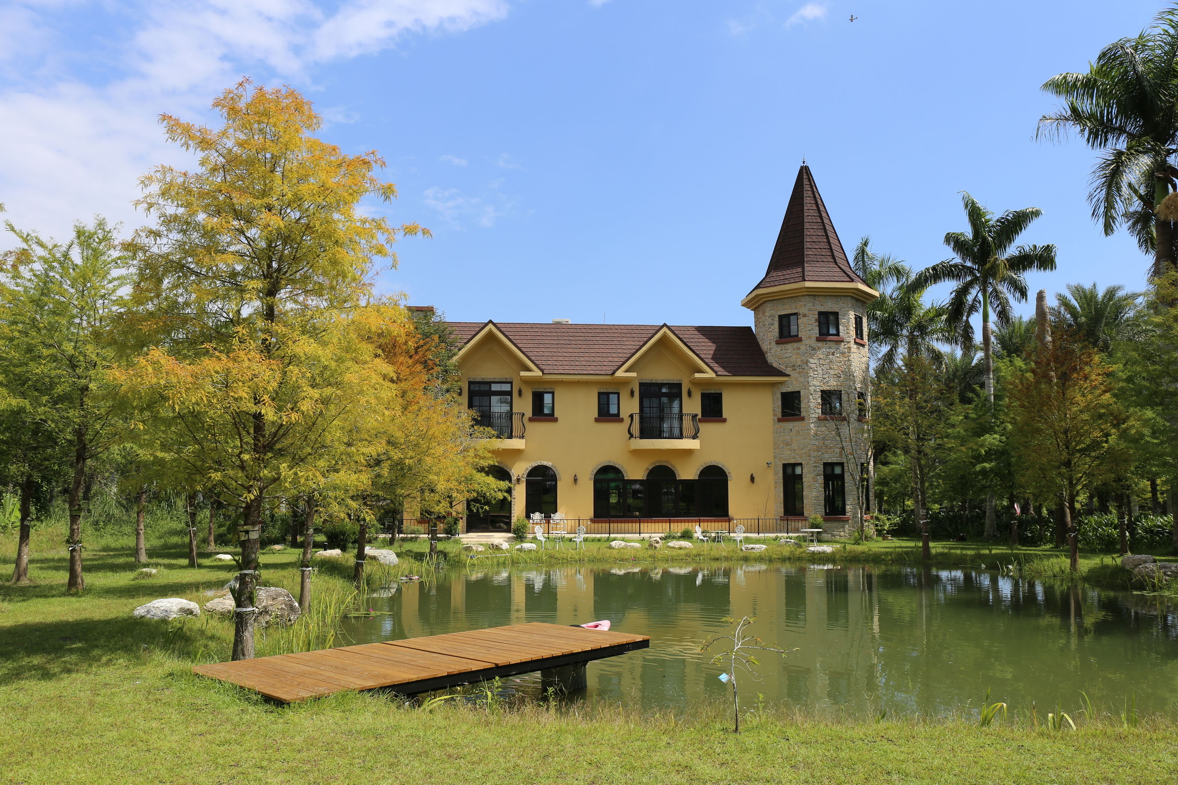 A large, yellow building with a tower, surrounded by a pond and trees.
