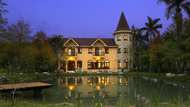 A large, multi-story building with a tower, reflecting in a calm body of water. - Yun Shan Shui Villa Home (Shoufeng)