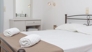 Una cama bien hecha con sábanas blancas y dos toallas enrolladas sobre una mesita de noche marrón.