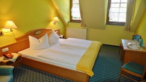 Une chambre d’hôtel comprenant un lit, une table de chevet, une lampe, une chaise et un bureau avec une autre chaise.